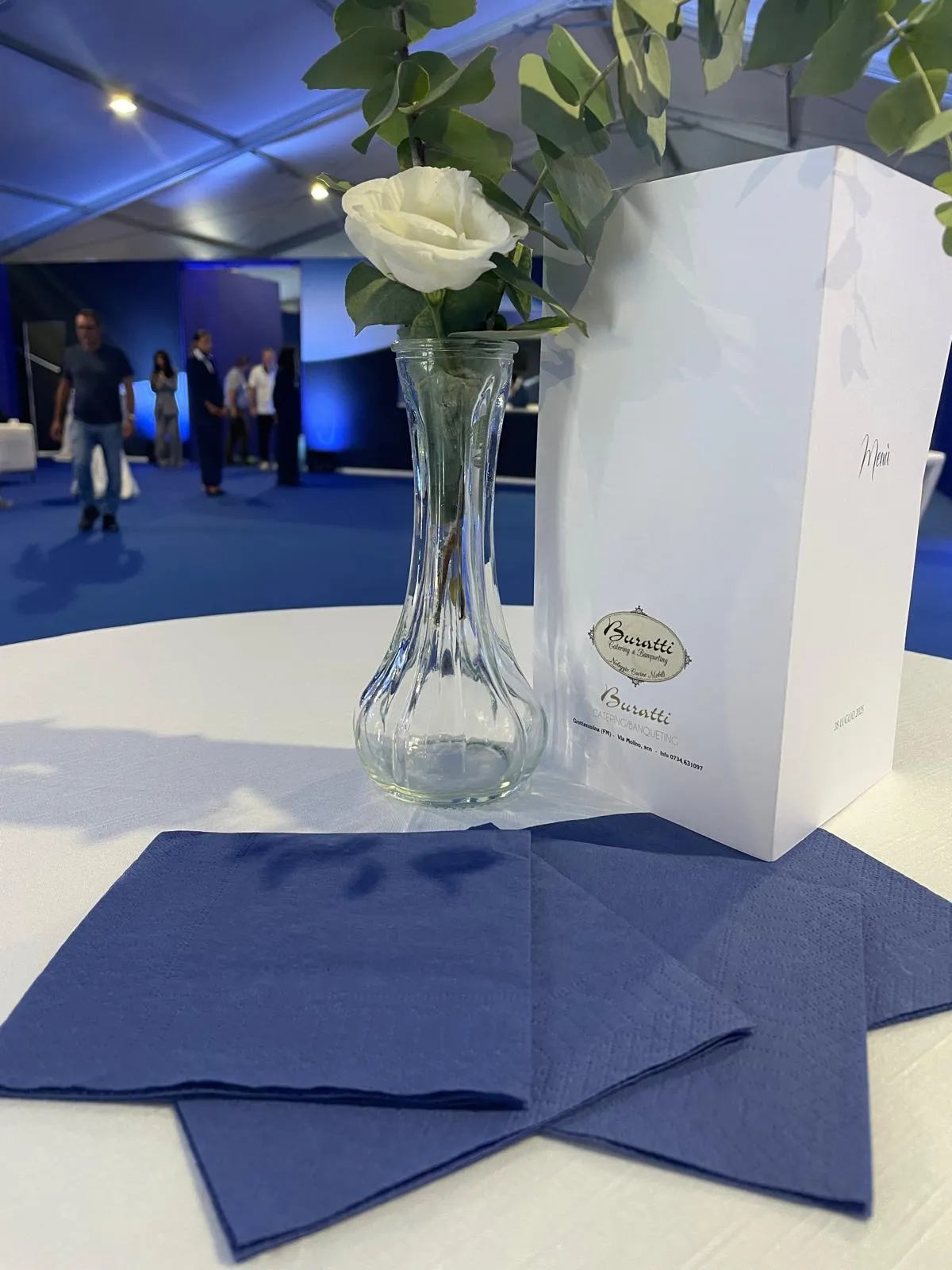 Centrotavola con fiore bianco, eucalyptus e menu appoggiato su tovaglioli blu