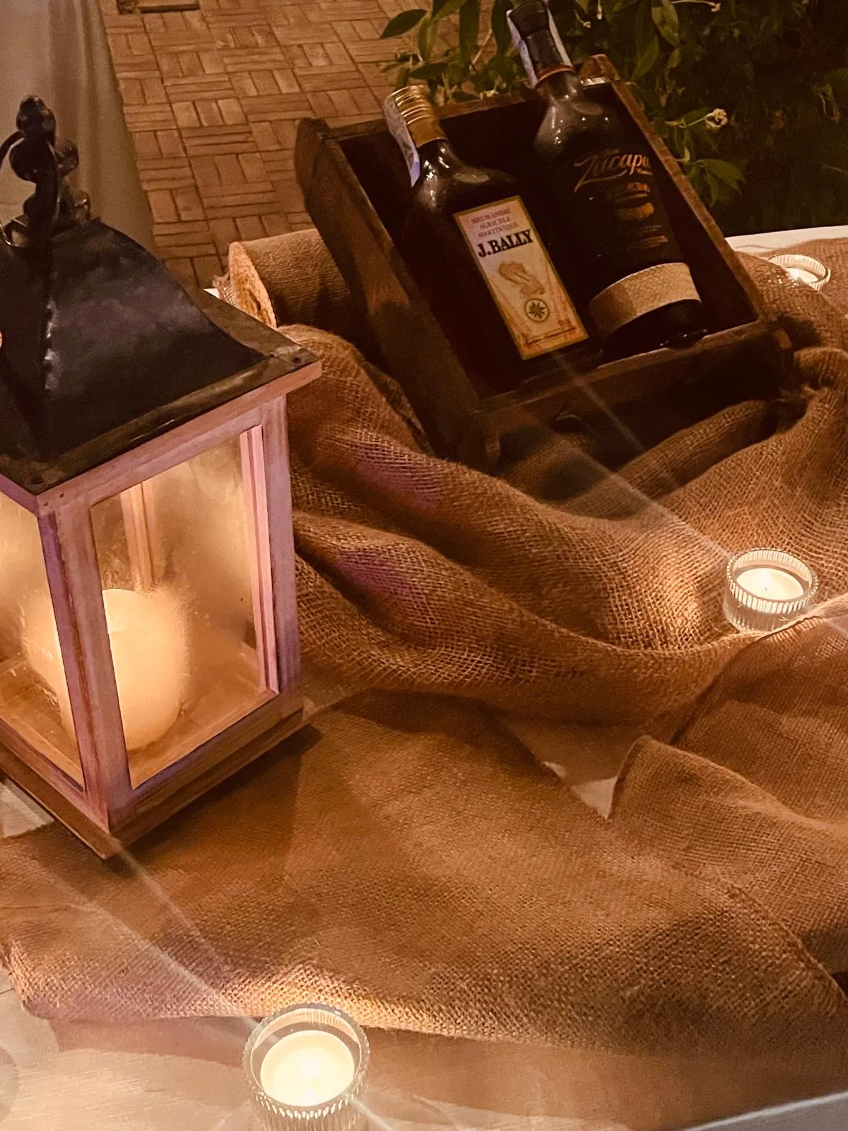 Lanterna decorativa, bottiglie di rum e candele su tessuto rustico