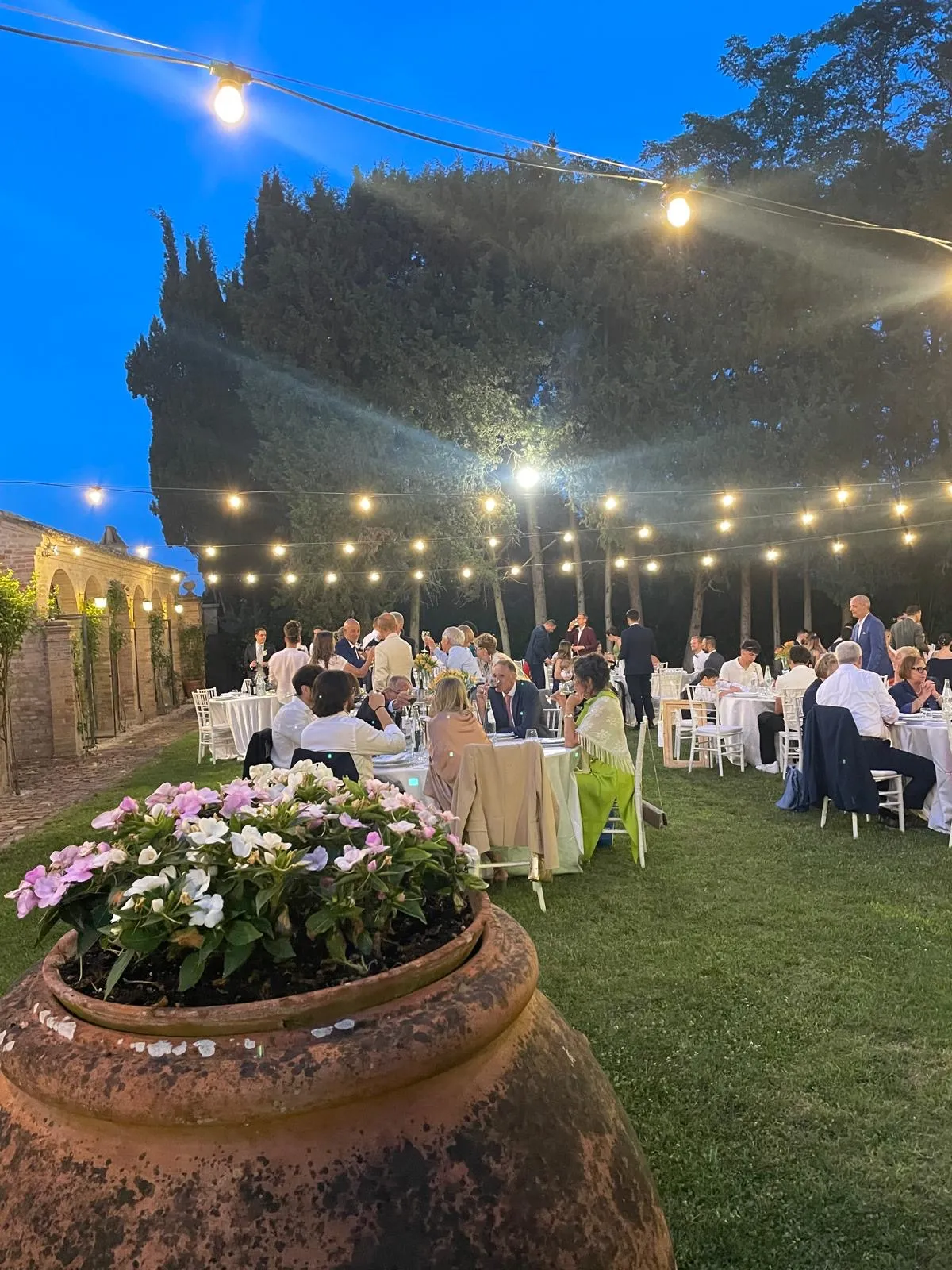 Cena all'aperto di sera con luci sospese e ospiti ai tavoli