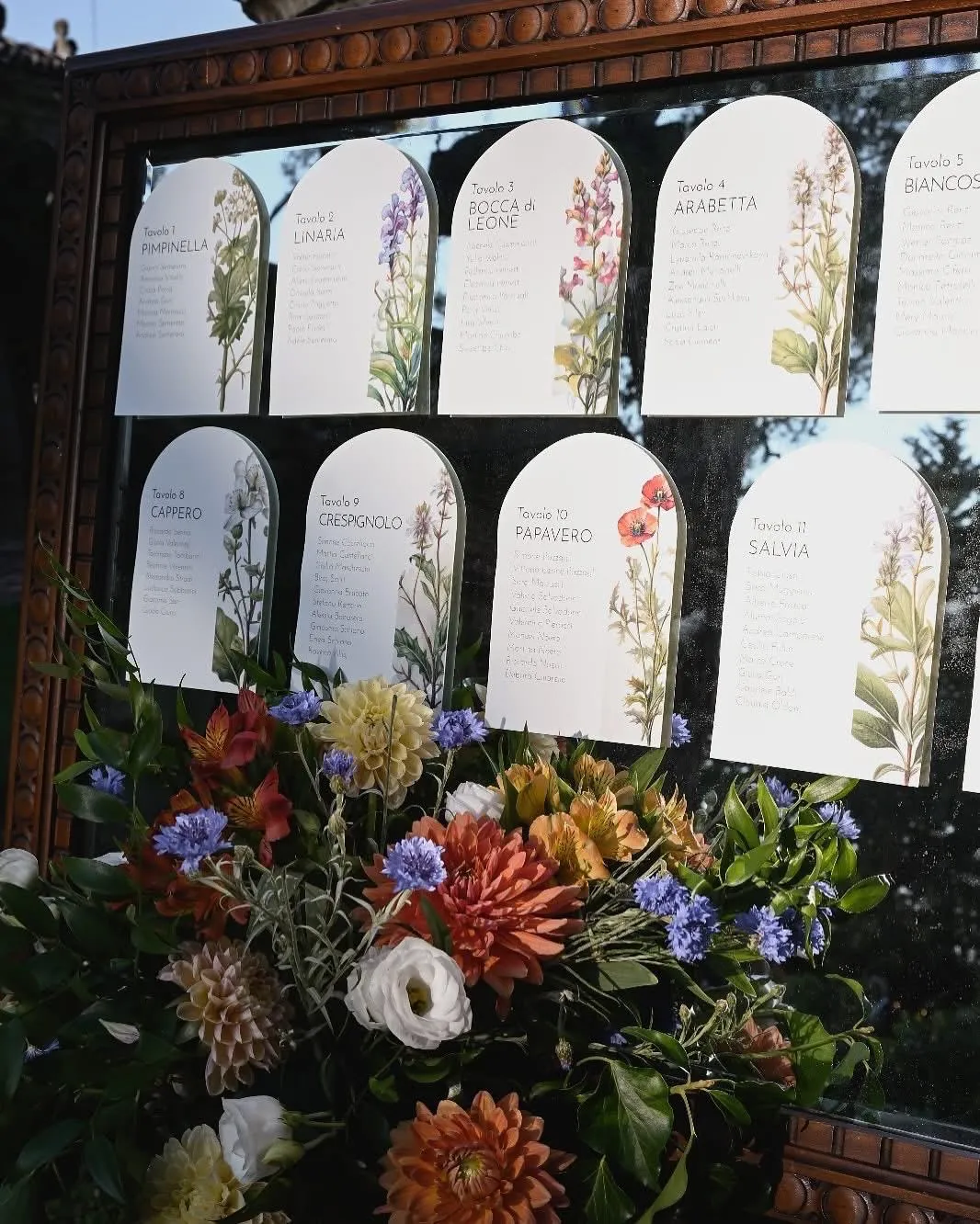 Tableau de mariage botanico con cartoncini dei tavoli e grande composizione di fiori freschi curato per evento Buratti Catering