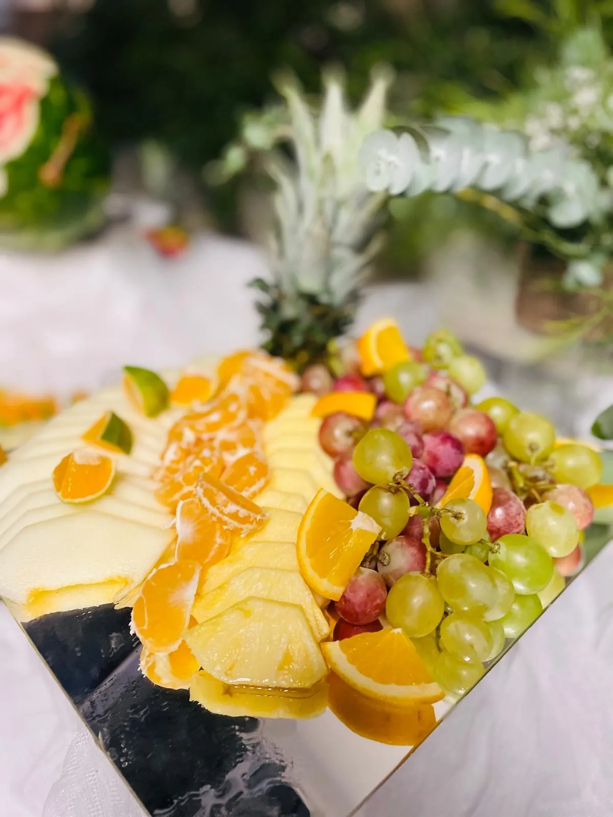 Vassoio di frutta fresca con ananas, agrumi e uva su piatto a specchio allestito da Buratti Catering