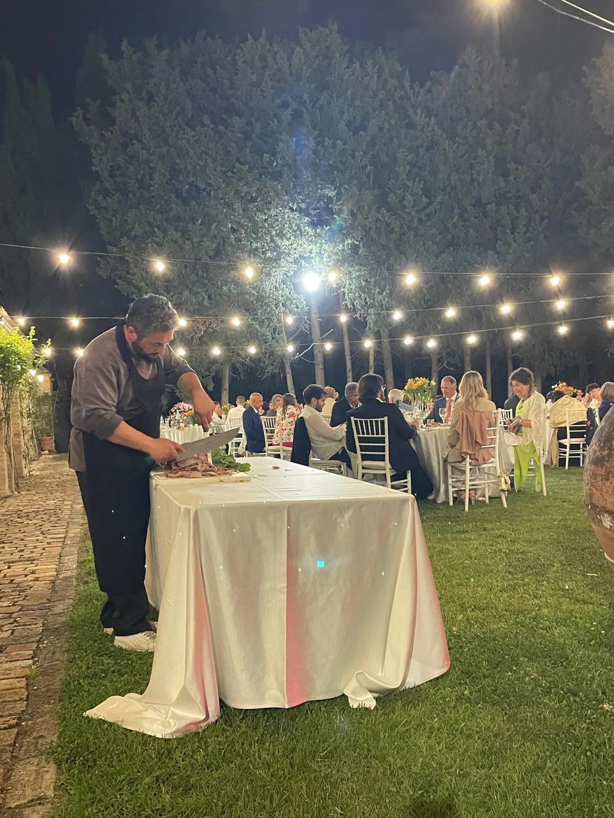 Chef Buratti Catering che affetta carne al taglio su tavolo all'aperto durante cena di matrimonio in giardino