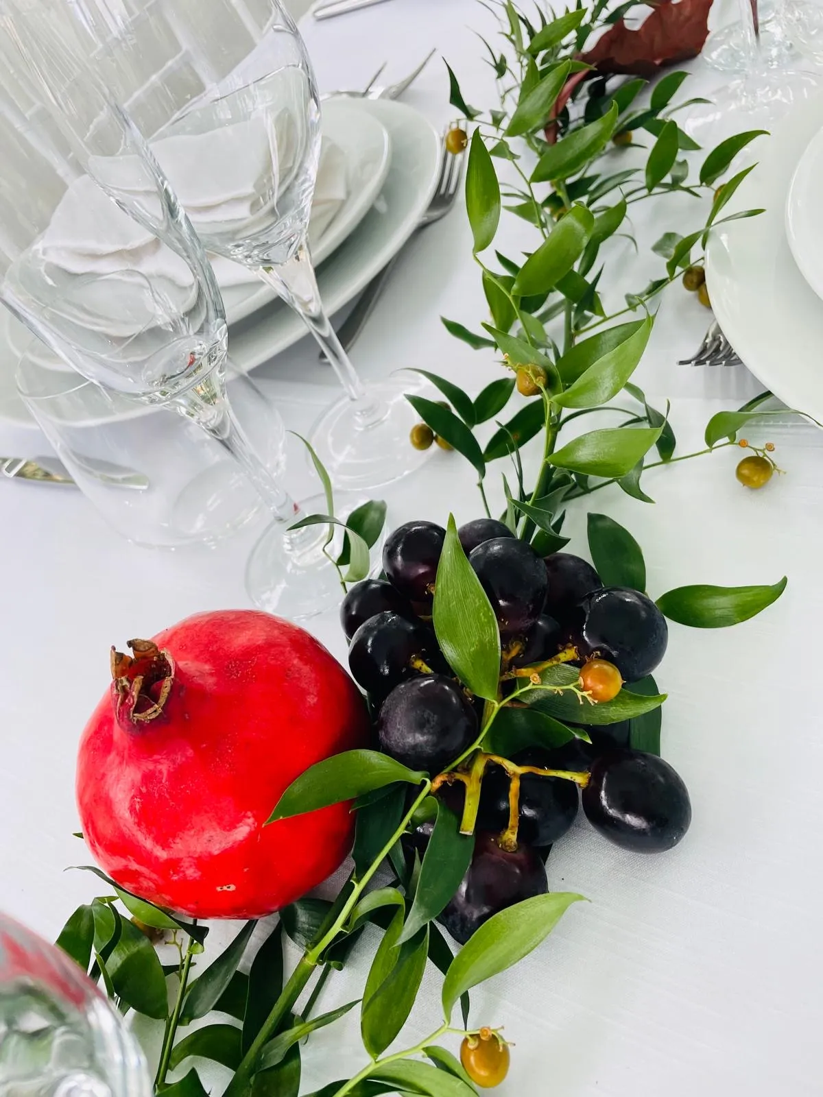Centrotavola con melograno rosso, uva nera e verde decorativo su tovaglia bianca per ricevimento elegante