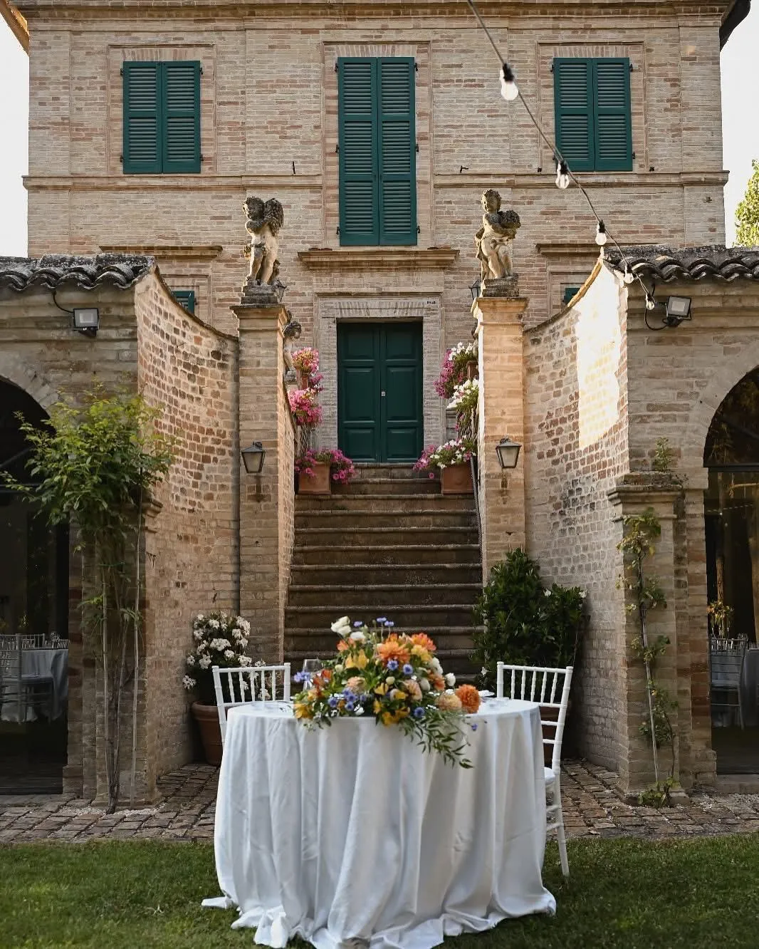 Tavolo rotondo con grande composizione floreale posizionato davanti a villa storica in mattoni per ricevimento di nozze