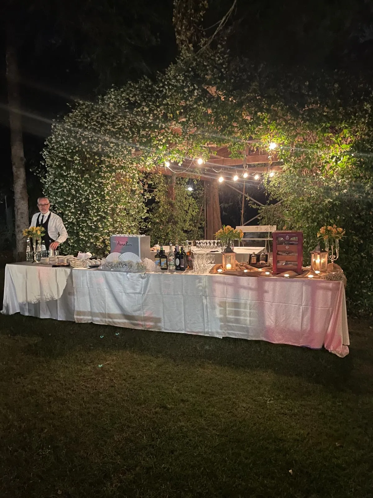 Bancone bar allestito all'aperto con luci serali e barman al lavoro