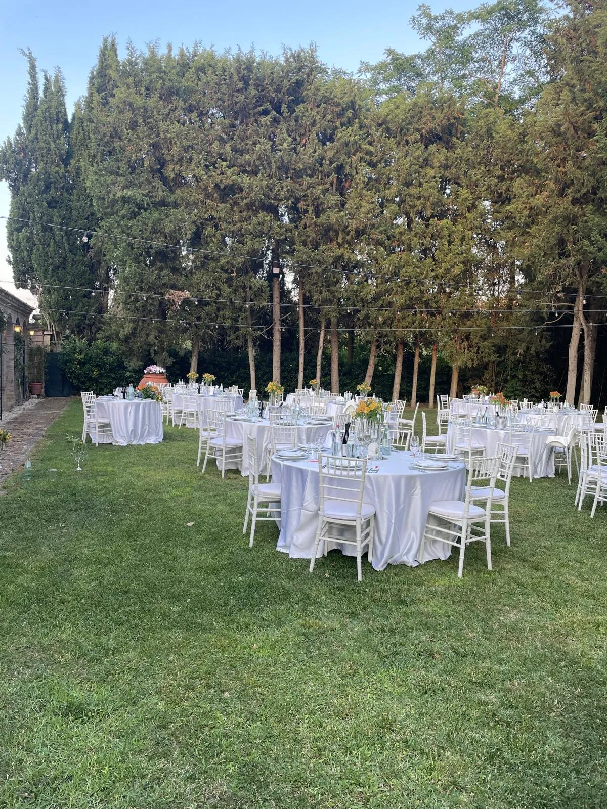 Allestimento giardino con tavoli rotondi apparecchiati e sedie bianche per ricevimento matrimonio all'aperto Buratti Catering