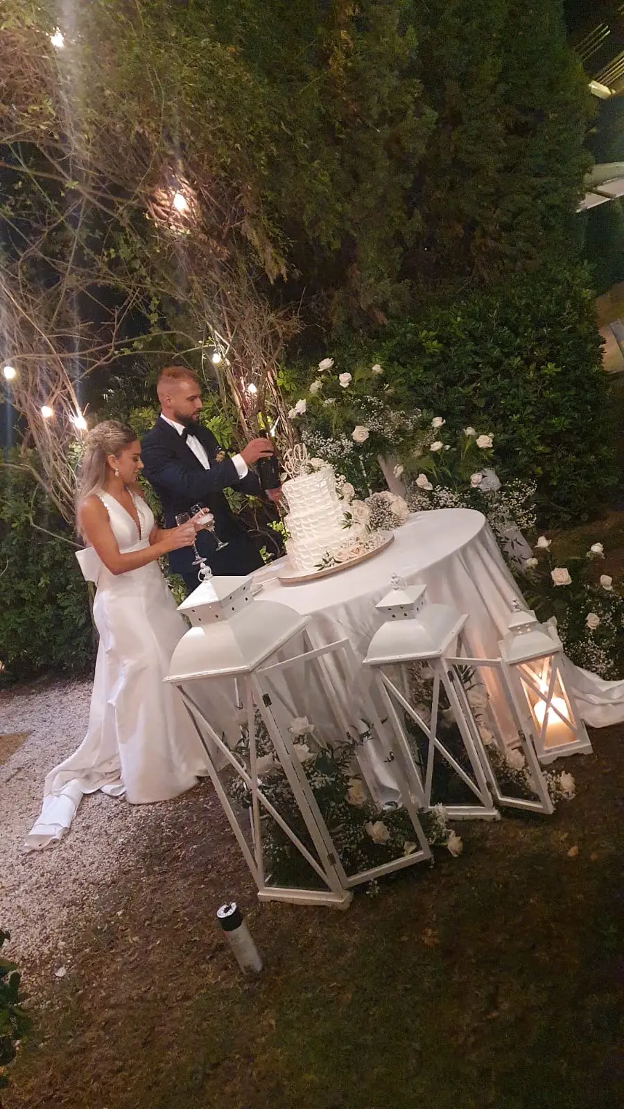Sposi che brindano accanto alla wedding cake tra lanterne bianche