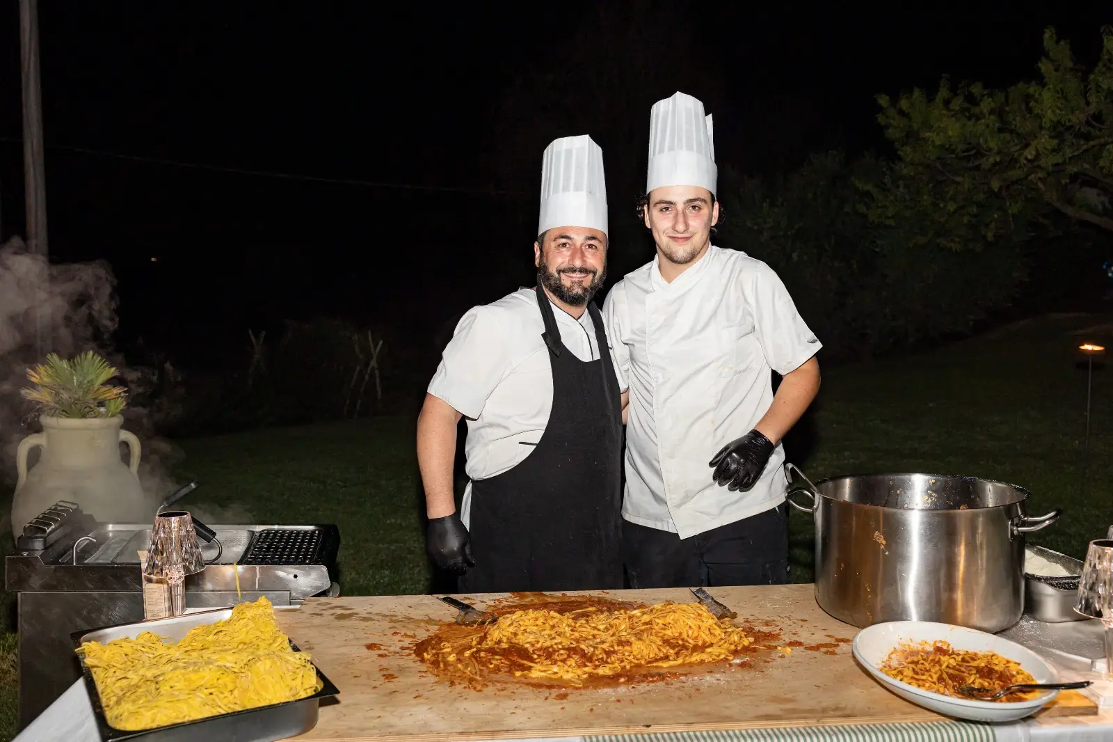 Due chef sorridenti alla postazione pasta durante il servizio serale