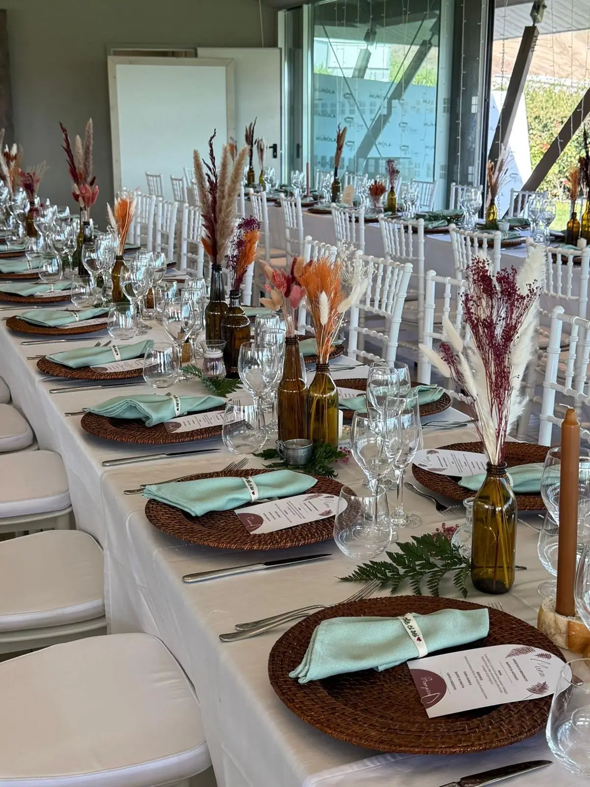 Tavolo imperiale interno con piatti in rattan, tovaglioli verde salvia e centrotavola naturali