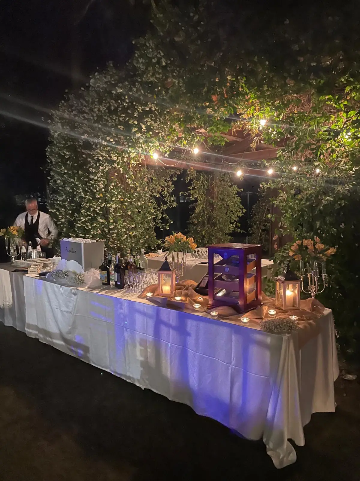 Buffet bar notturno sotto pergolato illuminato con candele e bottiglie
