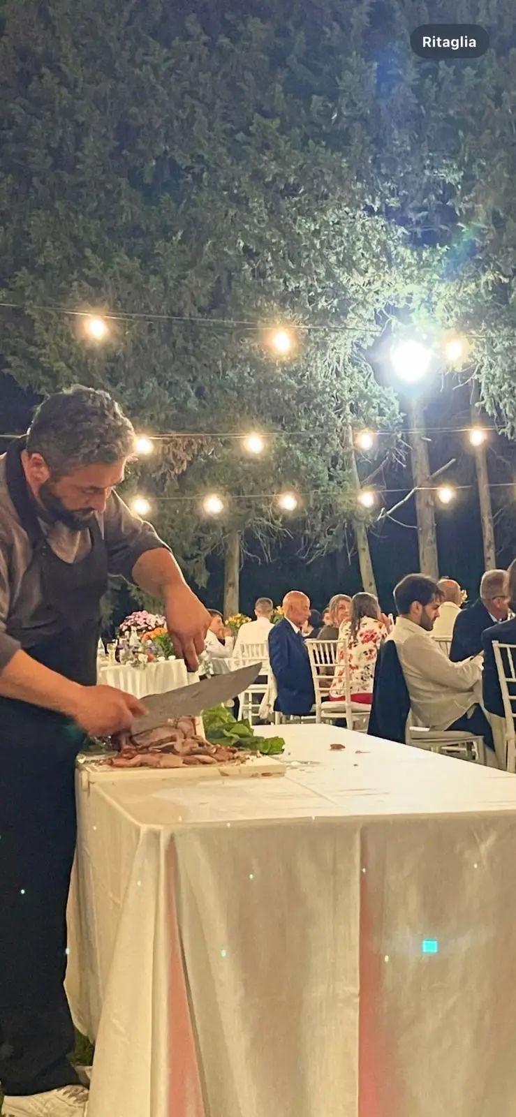 Chef che affetta carne al tagliere durante il servizio serale all'aperto