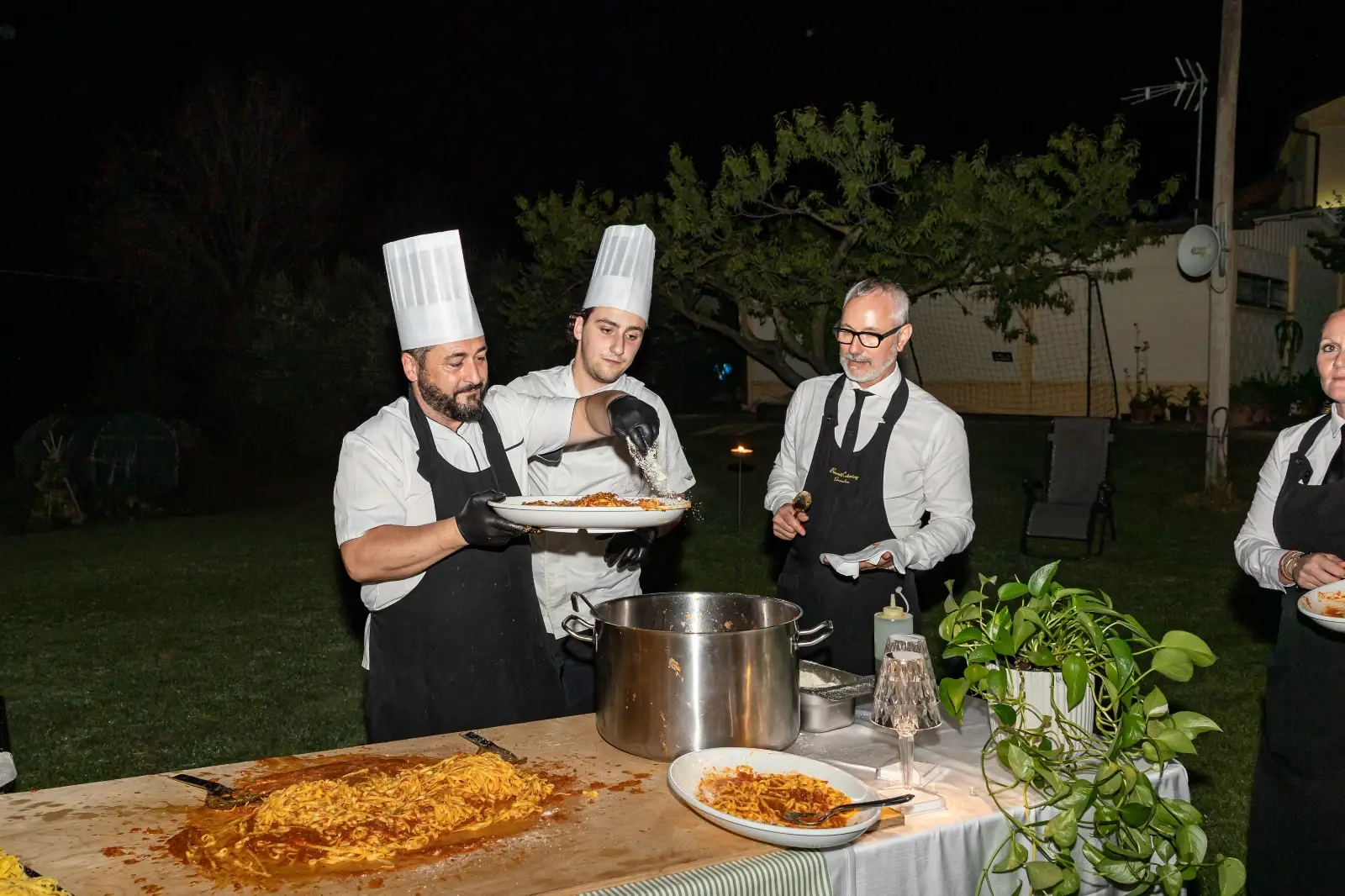 Chef che impiattano pasta fumante e la rifiniscono con formaggio davanti agli ospiti
