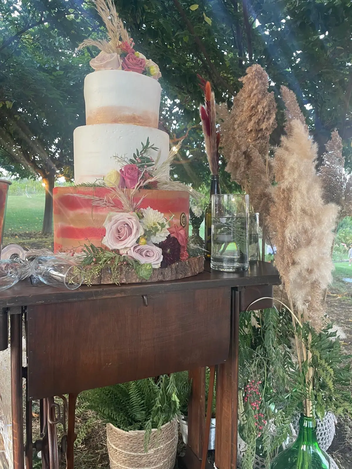 Torta nuziale decorata con fiori e pampas su tavolo vintage all'aperto