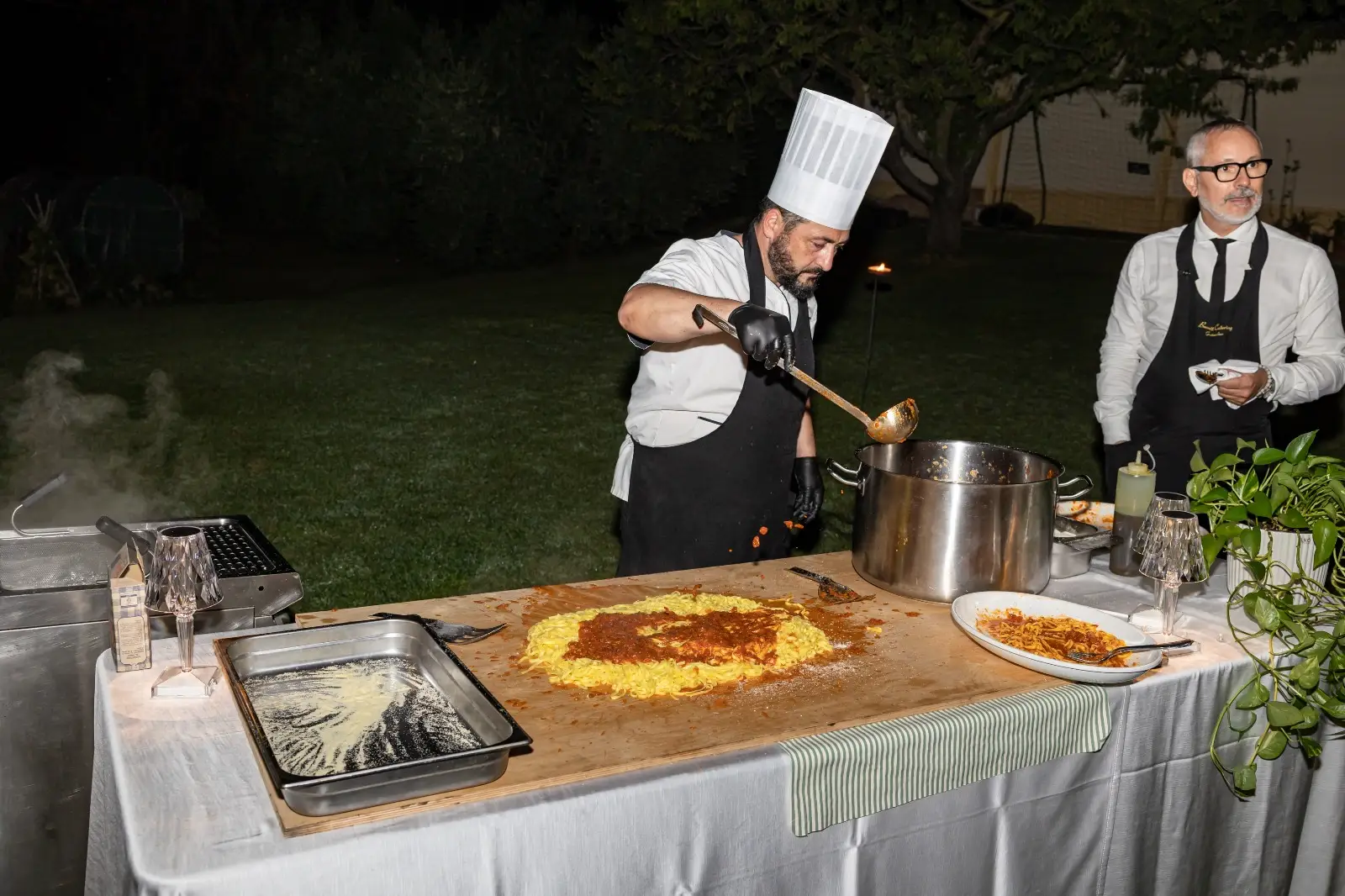 Chef che mantecano tagliolini alla lampada riscaldante durante il servizio serale