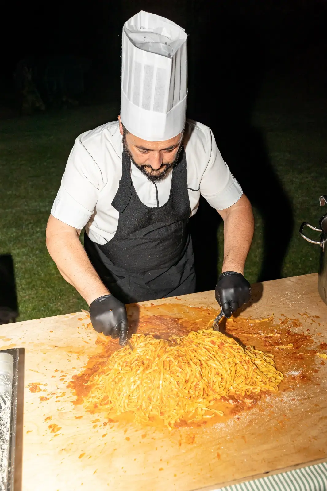 Chef che manteca tagliolini fumanti in pentola durante il servizio live