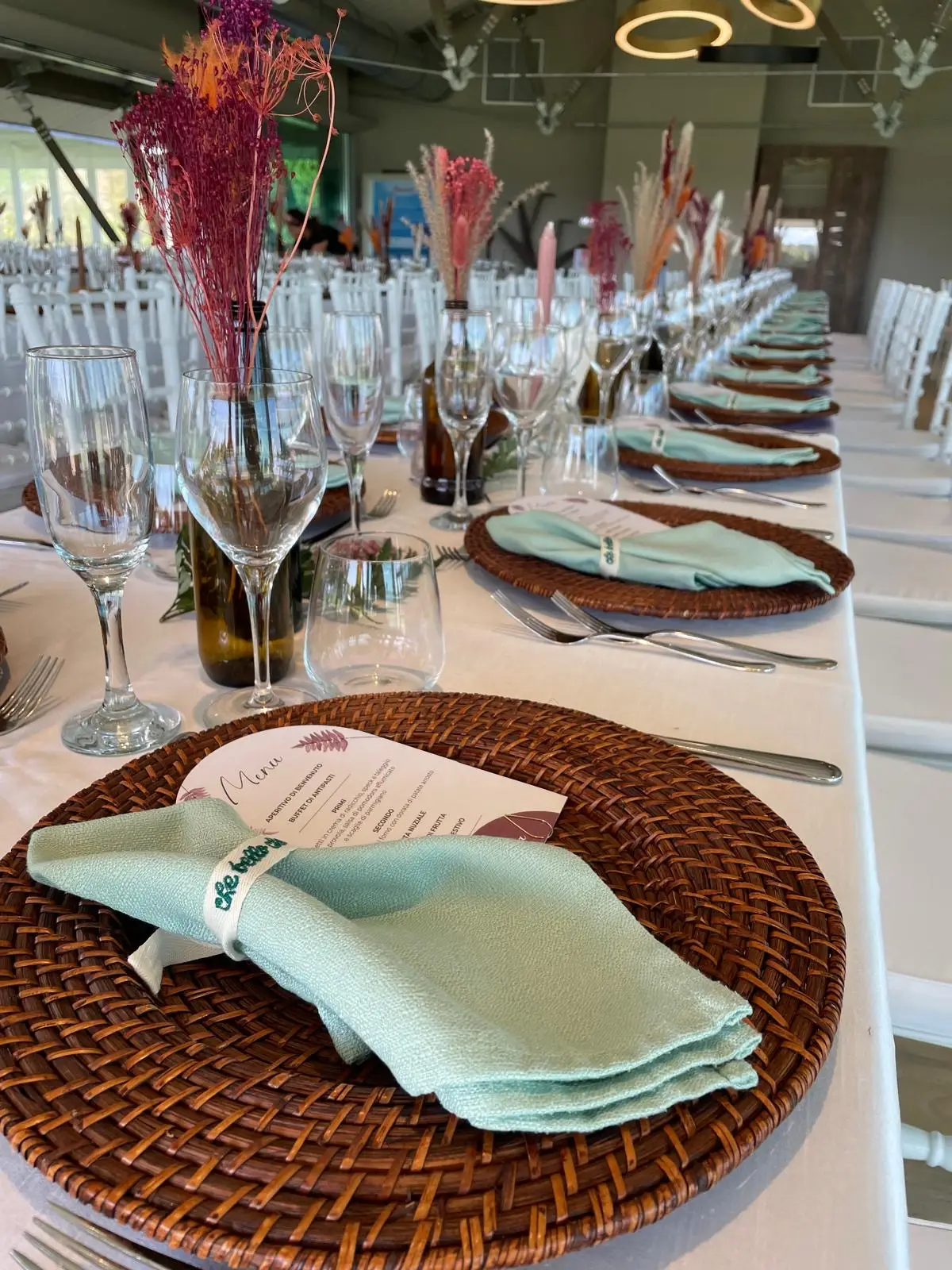Tavola apparecchiata con piatti intrecciati tovaglioli verde salvia e centrotavola naturali