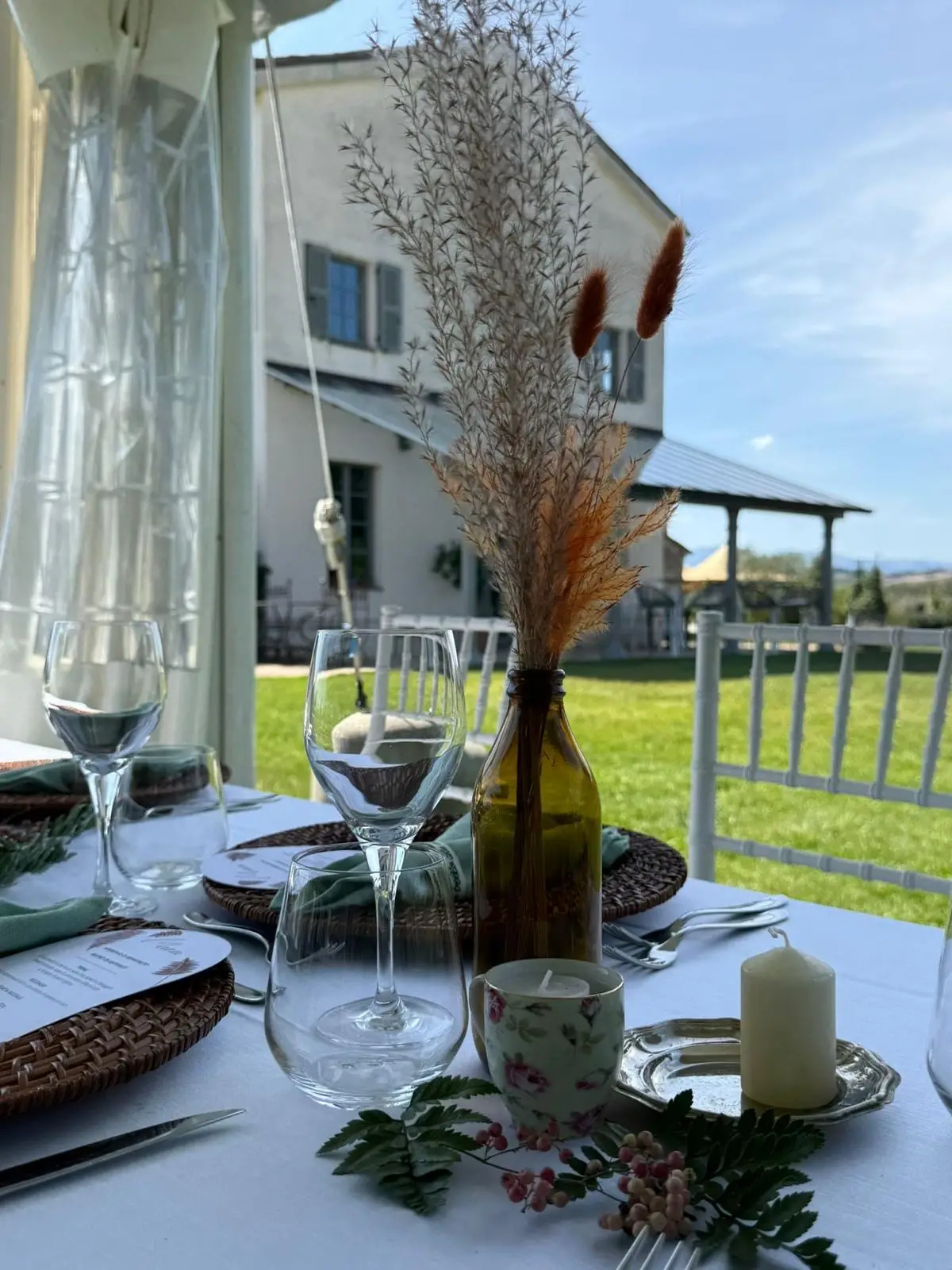 Dettaglio tavolo con bottiglia ambrata candela accesa e villa sullo sfondo