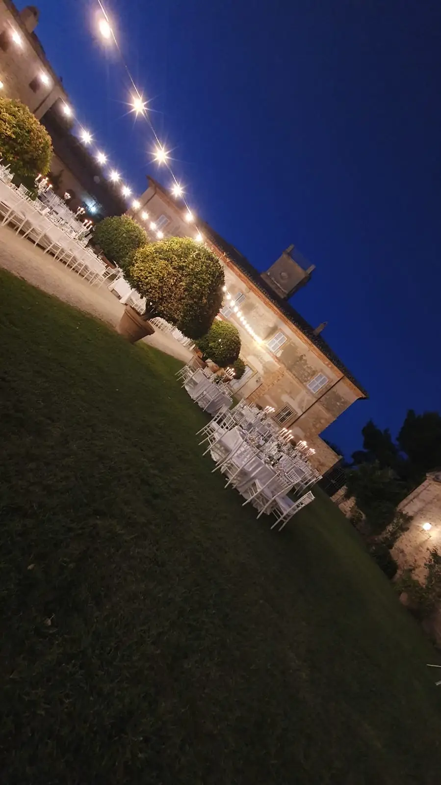 Villa illuminata di notte con tavoli apparecchiati e luci sospese in giardino