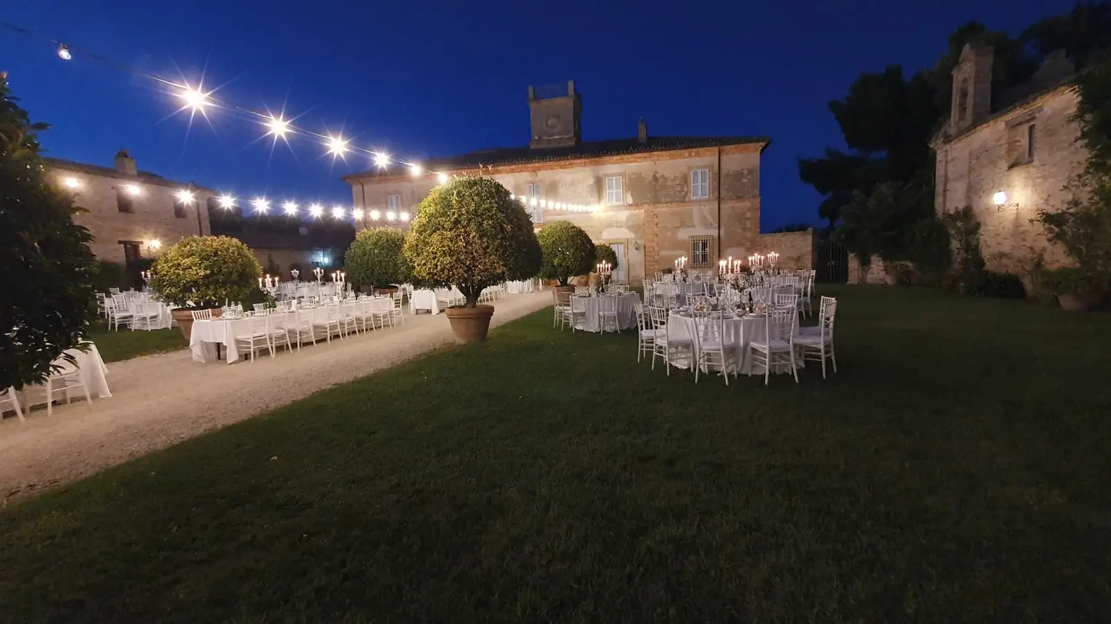 Villa illuminata di sera con giardino tavoli e atmosfera romantica