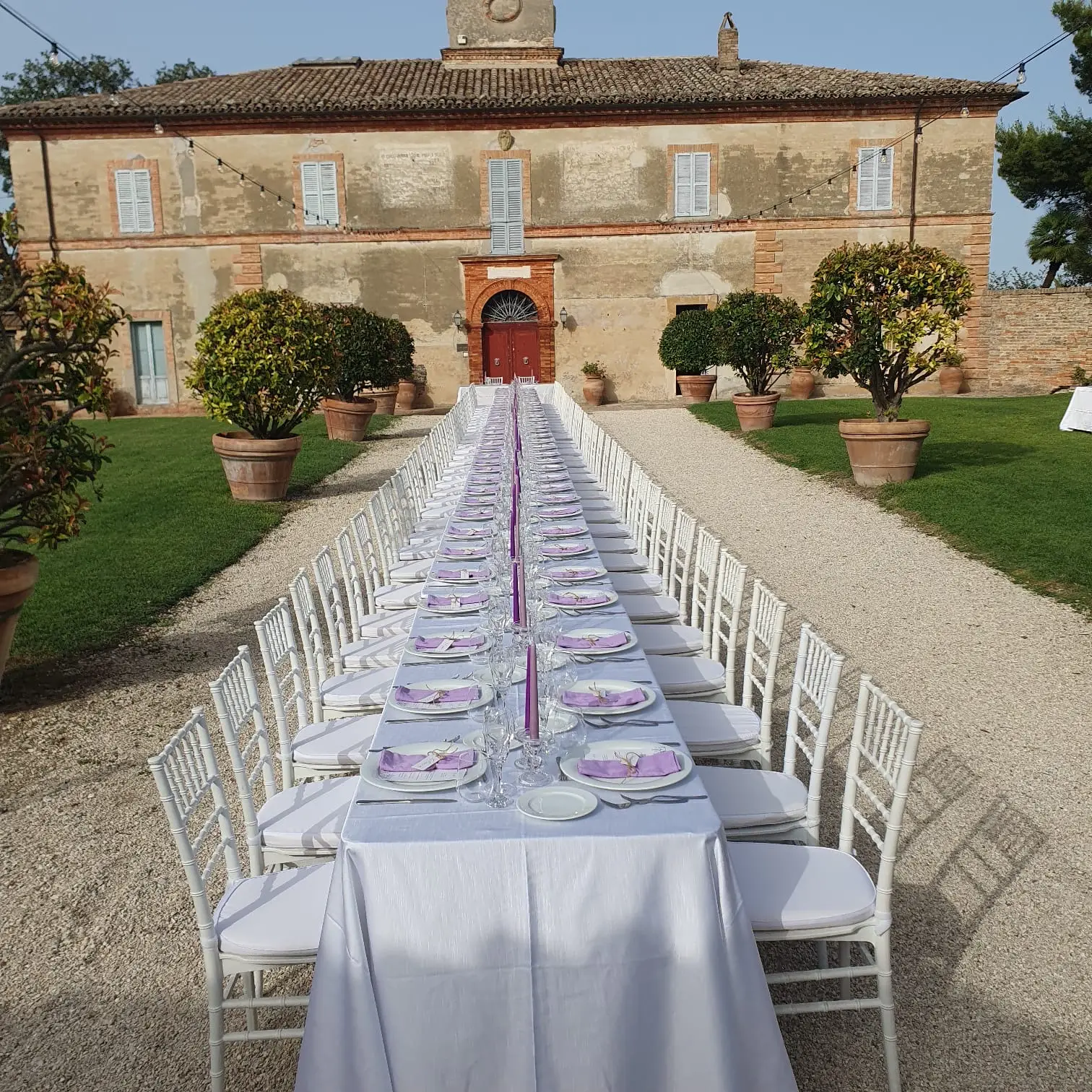 Tavolo apparecchiato in primo piano con villa storica sullo sfondo al tramonto
